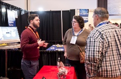 threepeoplespeakingtoeachotheratanexhibitbooth